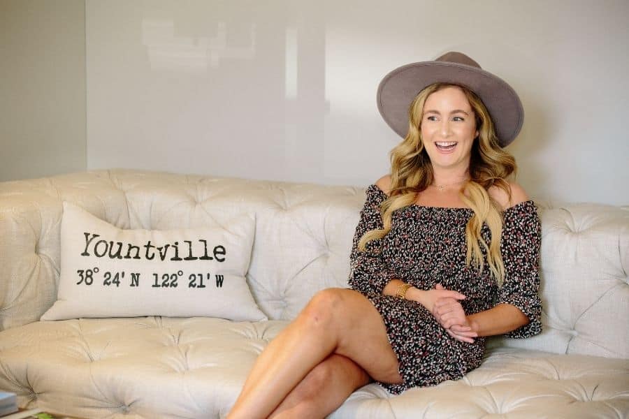 Blonde girl in a hat sitting on a couch with a yountville pillow