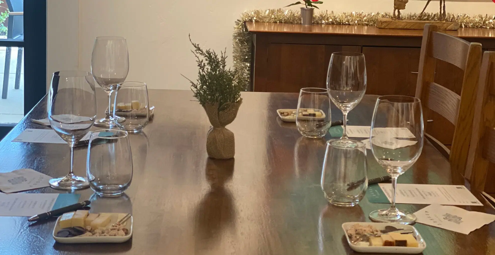 A wooden table set for 4 with wine glasses and small food pairing plates