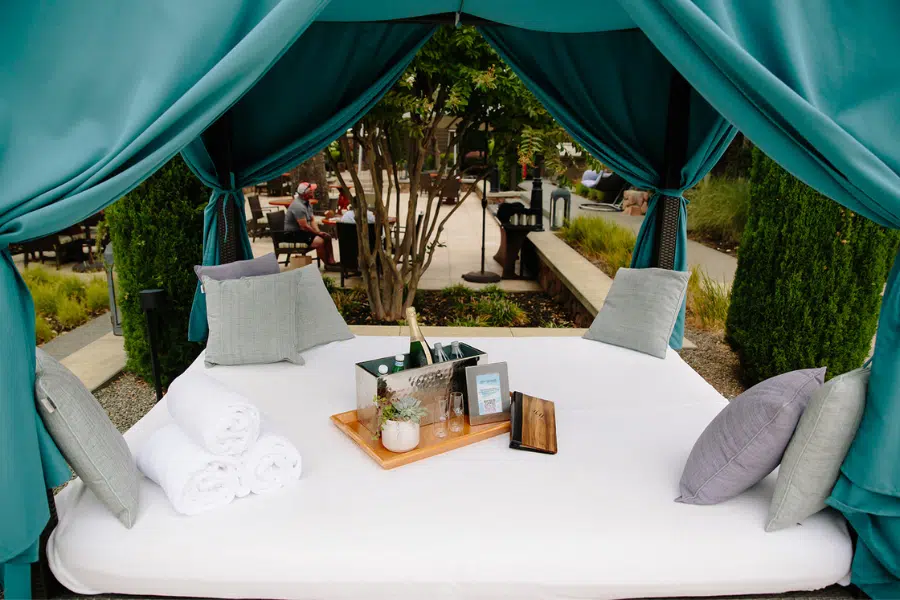 a cabana bed set with a tray of wine and food, pillows and curtains for privacy