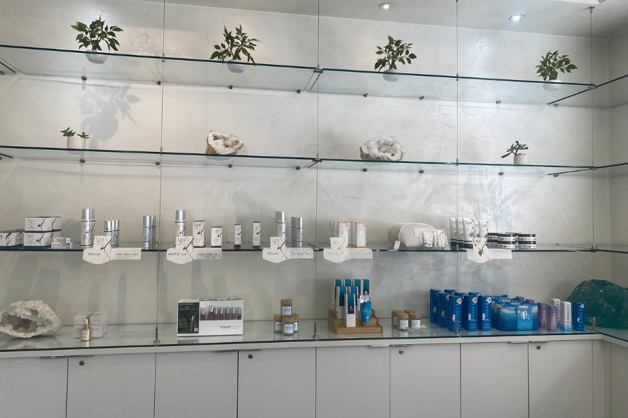 Glass shelves line a white wall filled with spa products, skin care, sun care