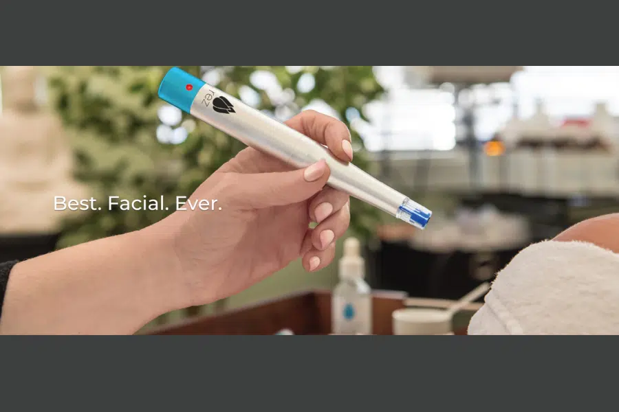 A womans hand holds a silver facial tool with a blue rubber tip on the end