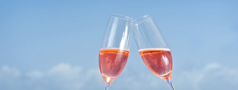 Two champagne glasses clink against a blue sky