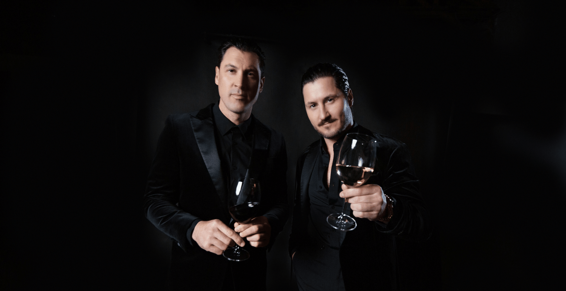 Photo of Chmerkovskiy brothers holding wine glasses, dressed in black suits against a black background
