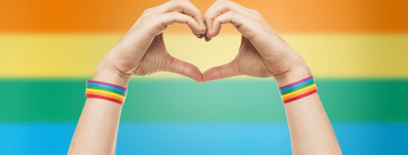 Hands making a heart shape in front of a rainbow flag