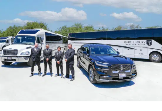 Men dressed in suits stand among several different vehicles including a bus, black sedan and a shuttle