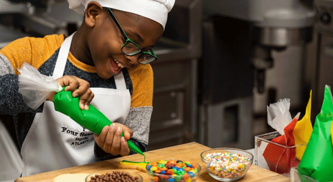 Four Seasons Childrens Cookies event kid decorating cookie with bowls of candy toppings infront of him